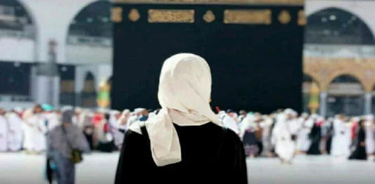 Person in white hijab facing Kaaba during Hajj pilgrimage, surrounded by worshippers in Mecca.