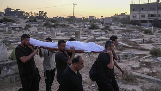 Men carrying a body on a stretcher through a cemetery at sunset